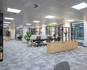 Contemporary CAT B workplace design featuring open-plan desks, biophilic planting, shelving dividers and neutral finishes in a refurbished commercial office.